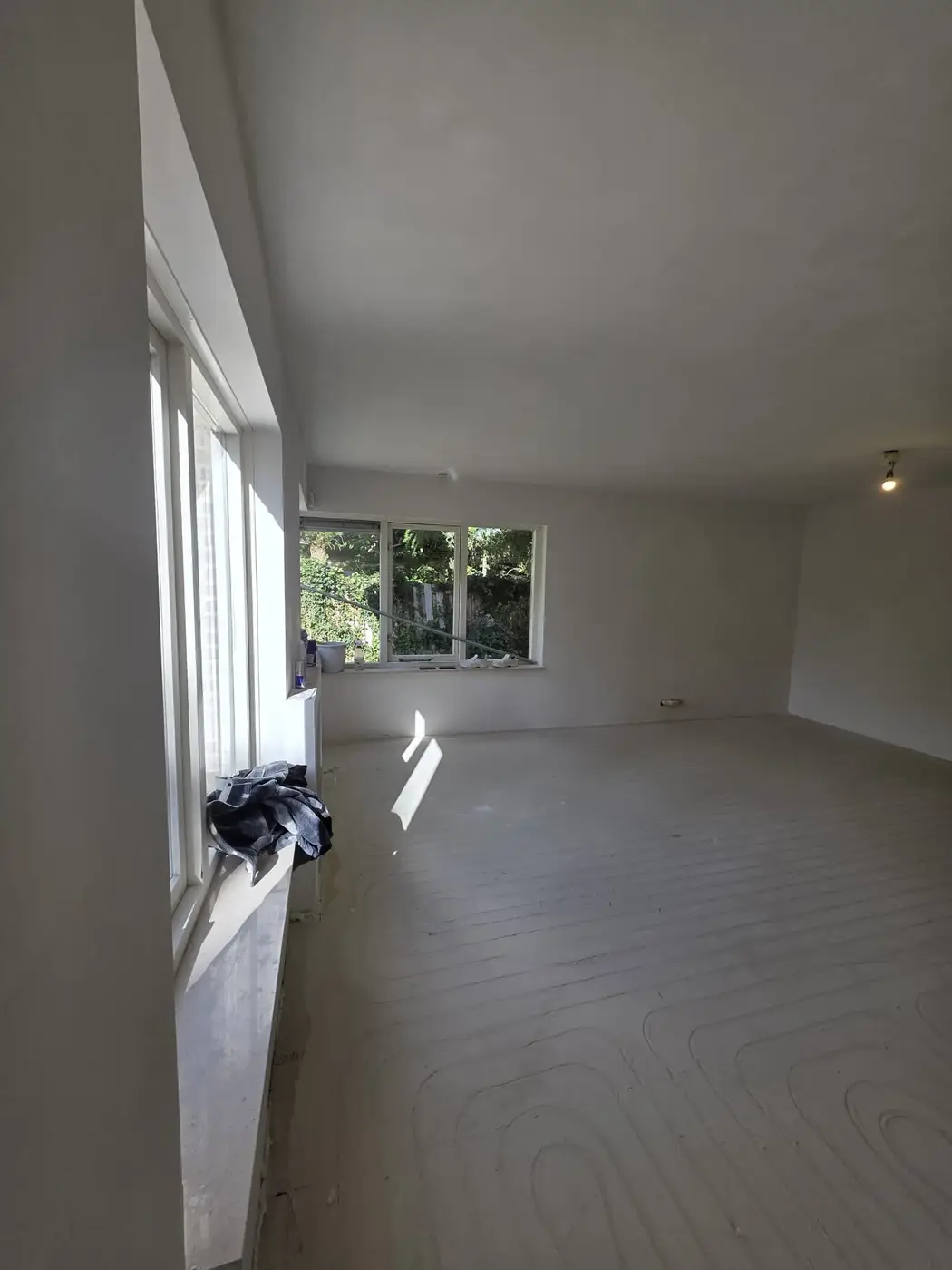 Lichte woonkamer met strak gestuukte wanden en naadloos plafond na renovatie