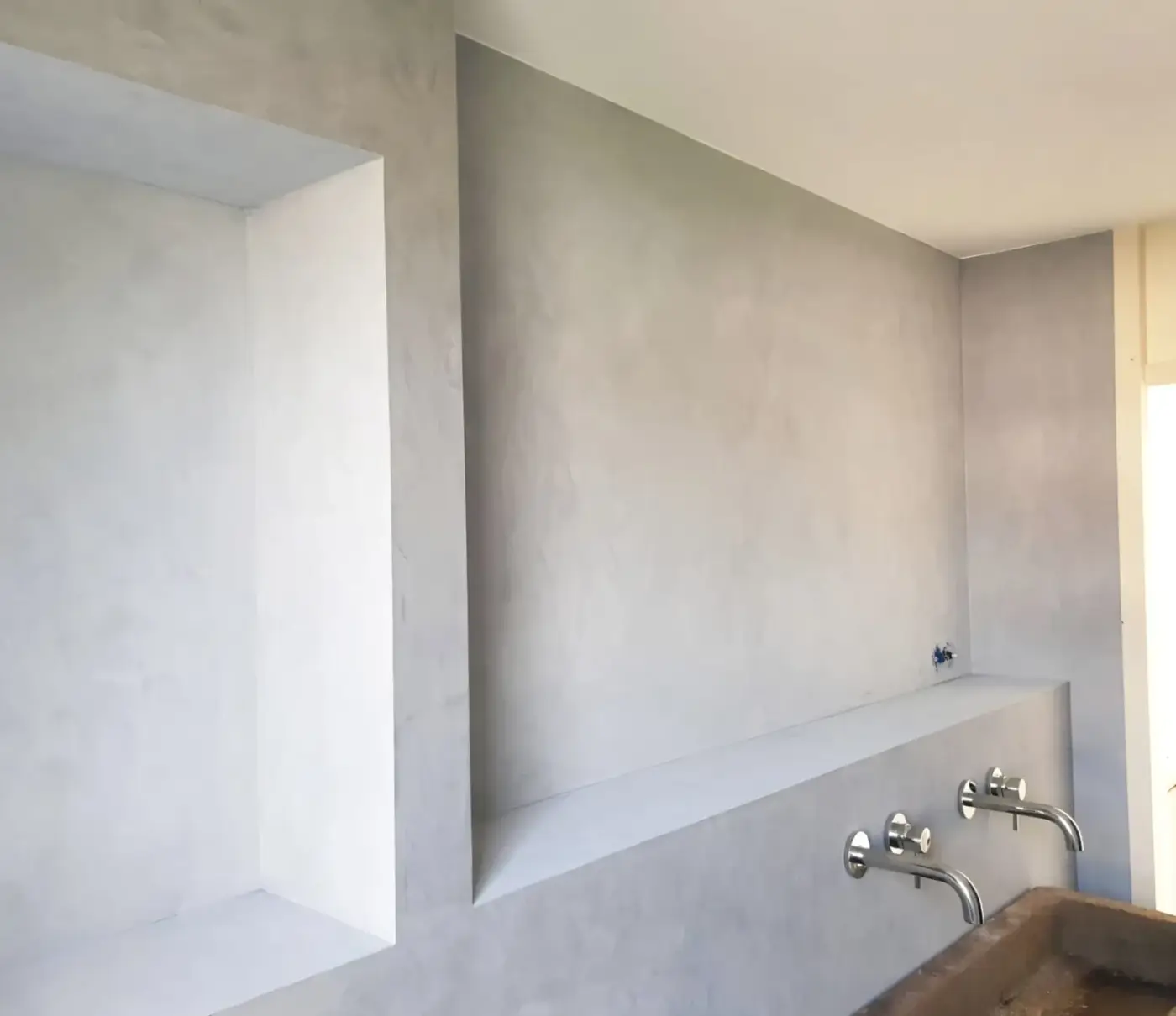 Badkamer met betonlook stucwerk, inbouwnissen en strakke wandplank