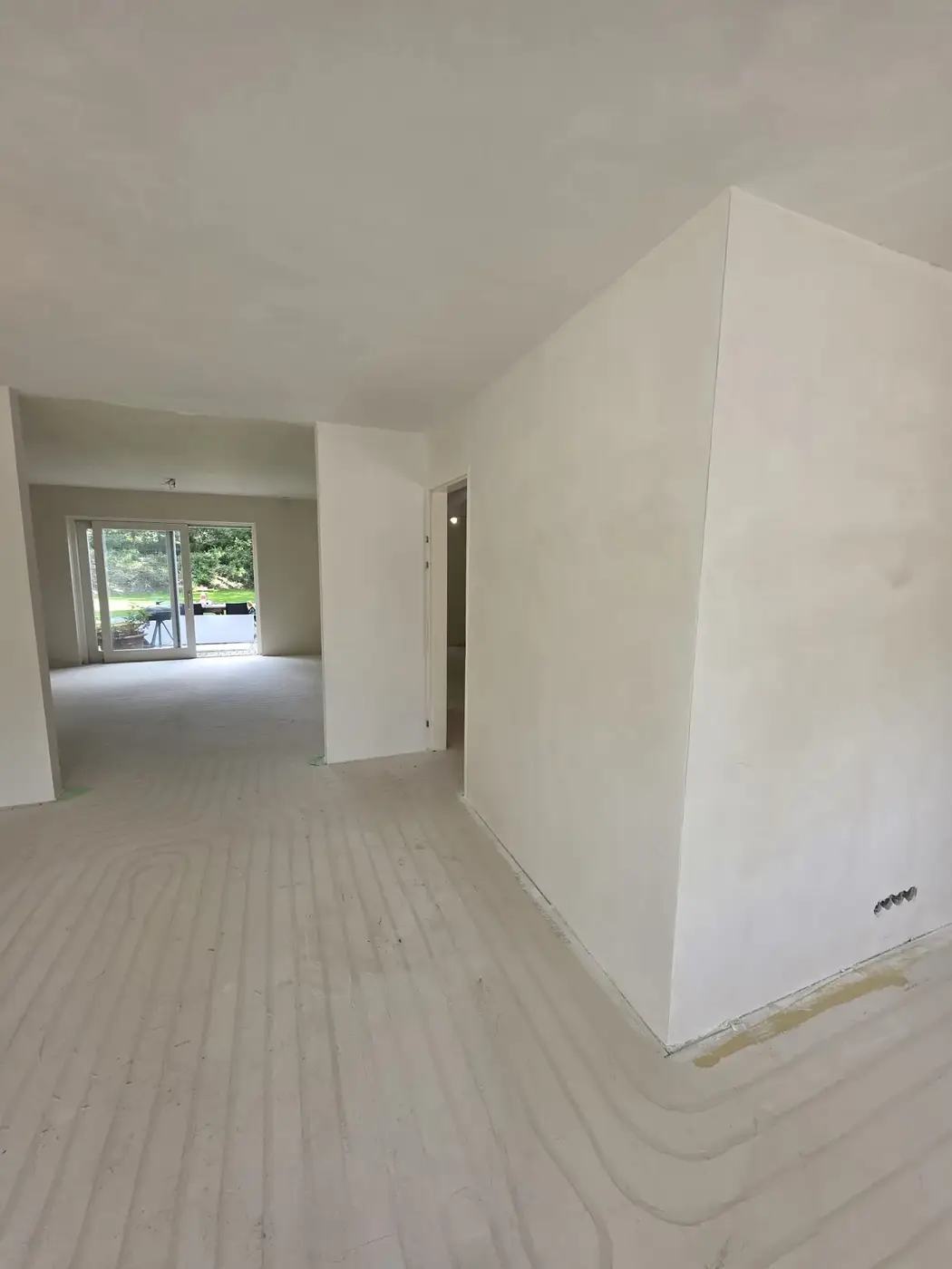 Open woonruimte met strak gestuukte hoek en doorgang naar de tuinkamer