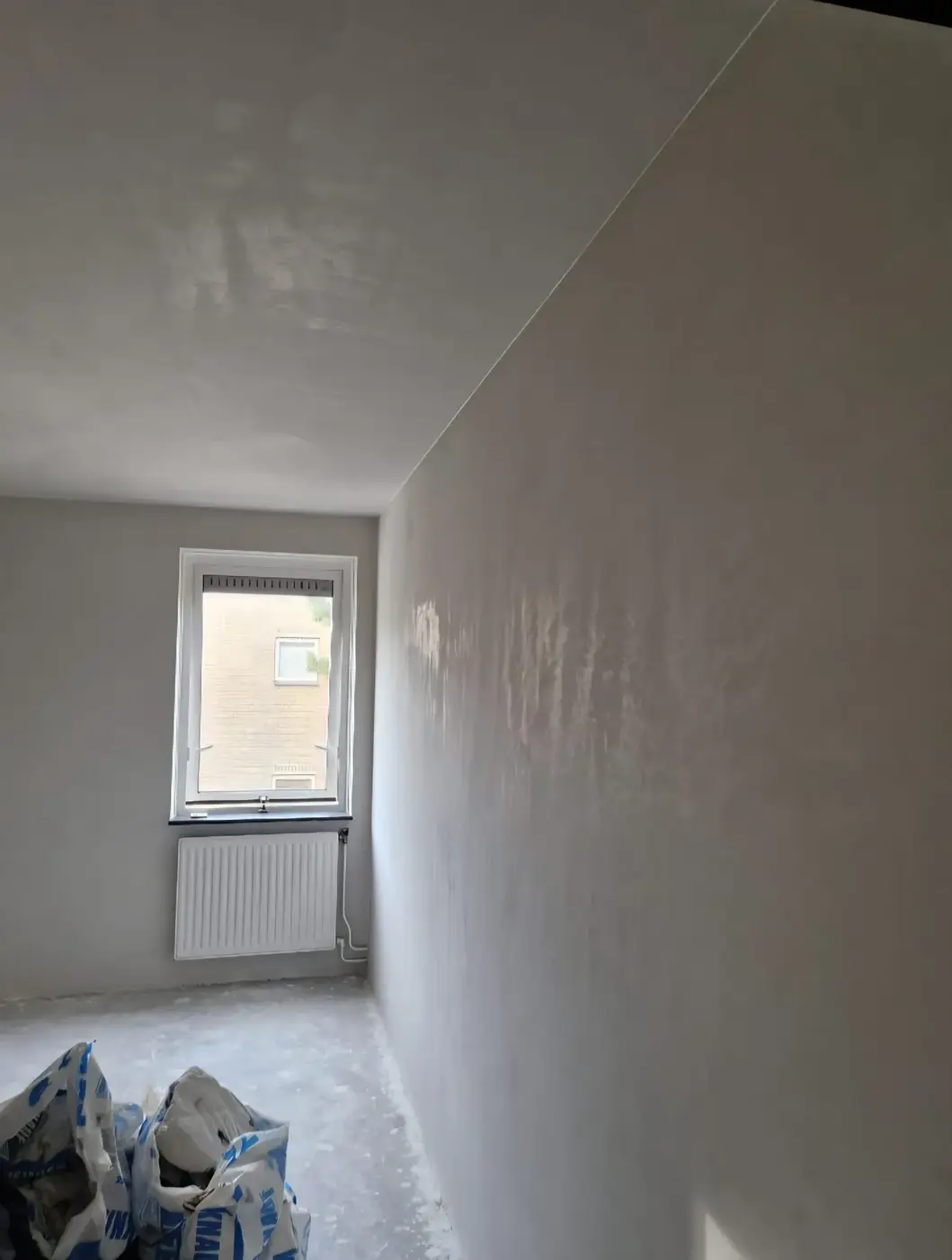 Lange slaapkamerwand en plafond spiegelglad gestuukt rond het raam